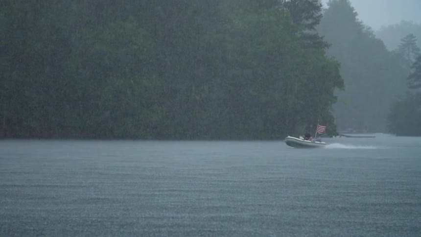 A couple of people in a boat on some water and it is raining or snowing