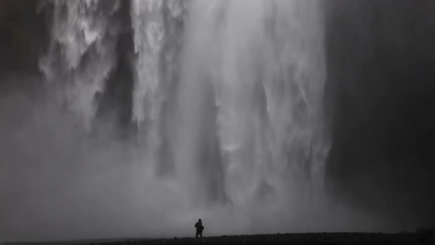 A person is standing near a huge waterfall