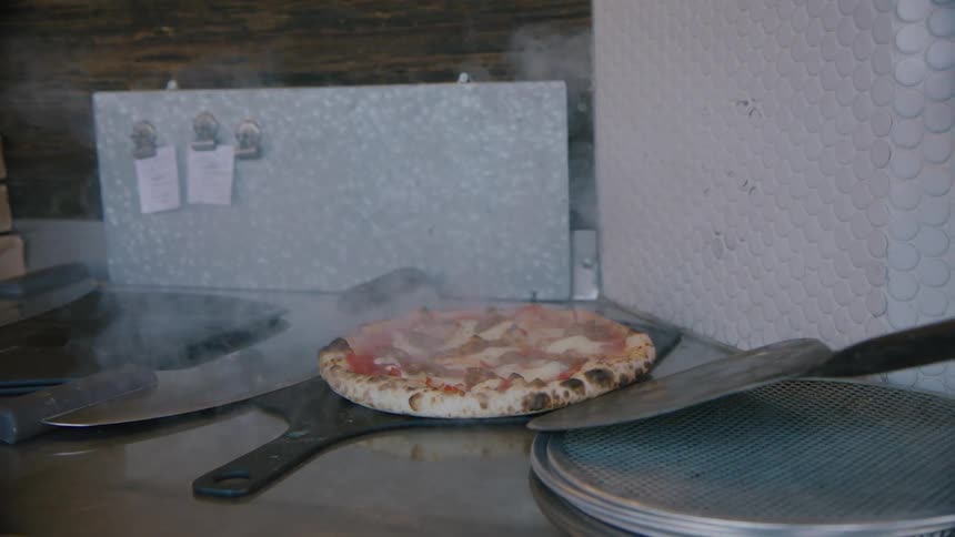 Someone takes a steaming pizza from the oven