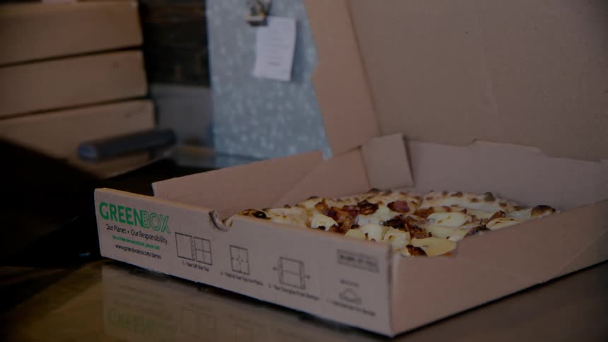 A pizza chef places a pizza in a box