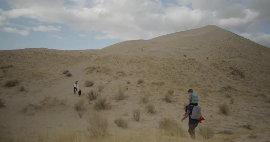 Three people and a dog are hiking up a desert hill