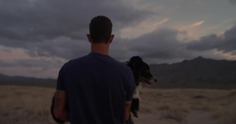 A man carries his dog through a field