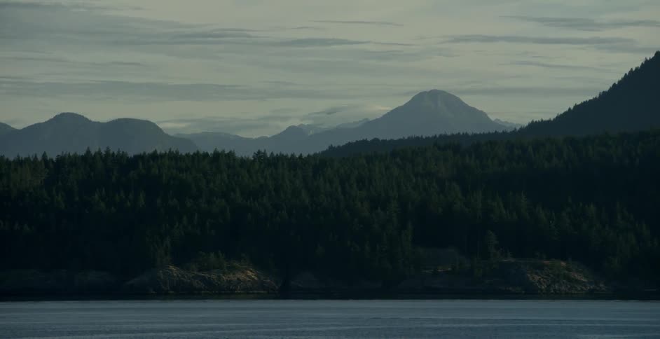 Lake in front of mountains and forest on cloudy afternoon