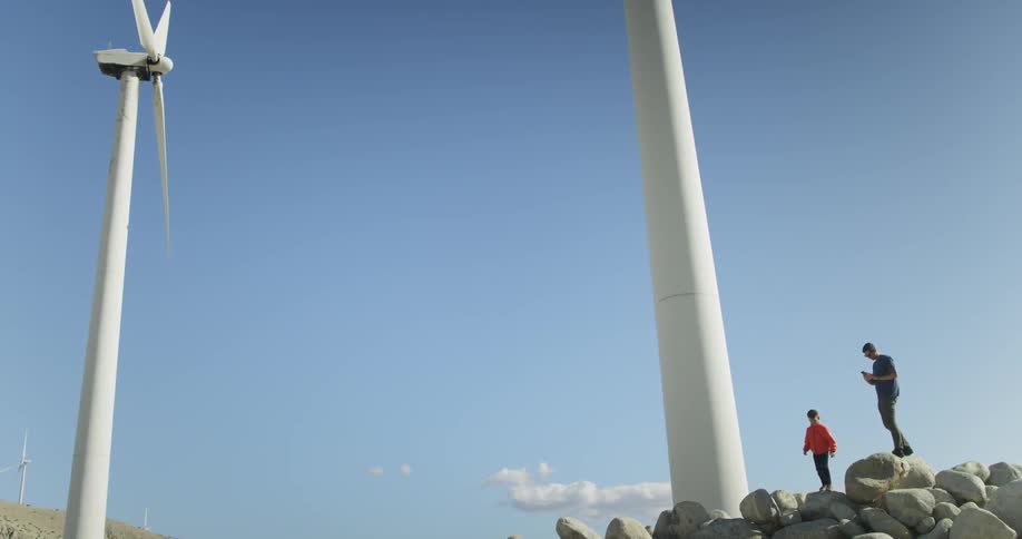 Two people jump on rocks near windmills