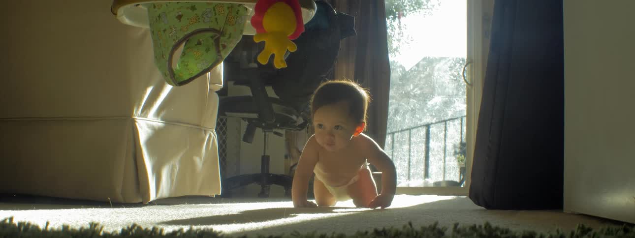A baby is crawling and exploring on a living room floor during the day