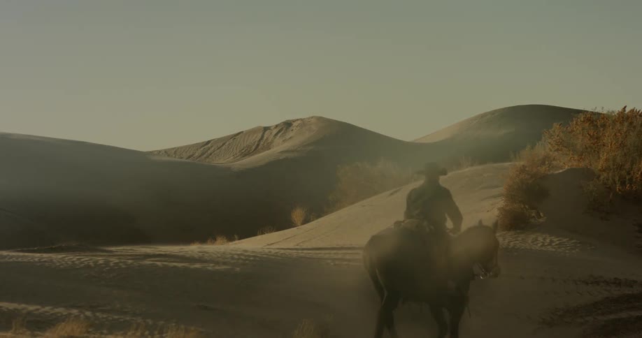 Man wearing cowboy hat riding horse over sand dunes