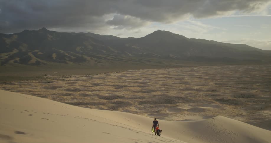 A dog walks beside a dad and son as they climb a sand dune