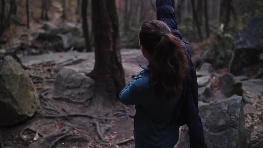 A woman puts on a jacket in a forest