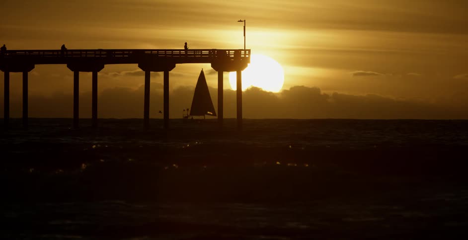 The suns setting on the water with a boat and a bridge in the foreground