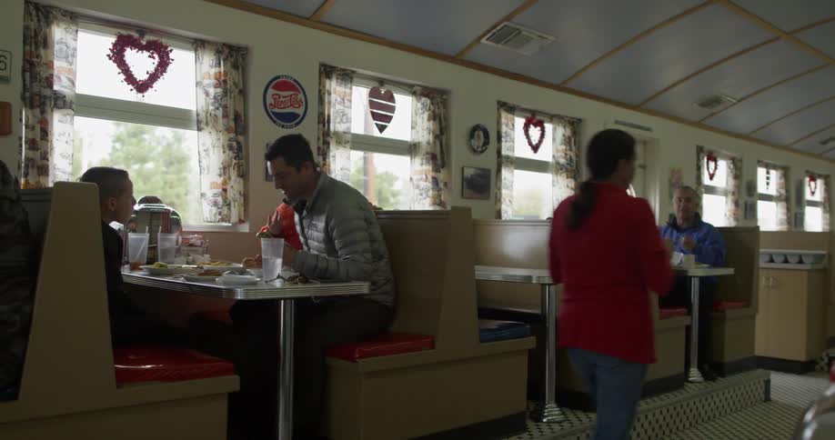 A man and two kids eating at a booth in a diner