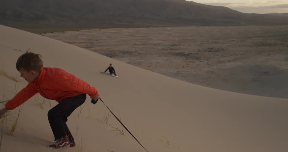 Two boys play on a sand dune in the desert