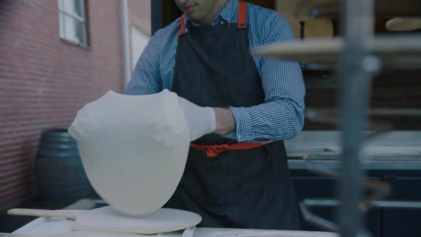 A man forms pizza dough and lays it on a wood paddle