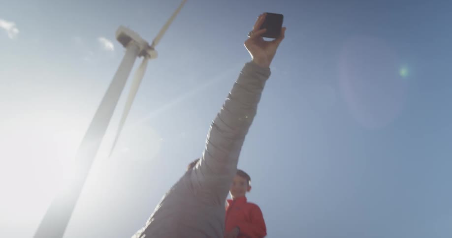 Man photographing himself with boy outside near wind turbines in sunny day