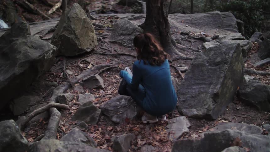 A woman squats down near rocks in the woods