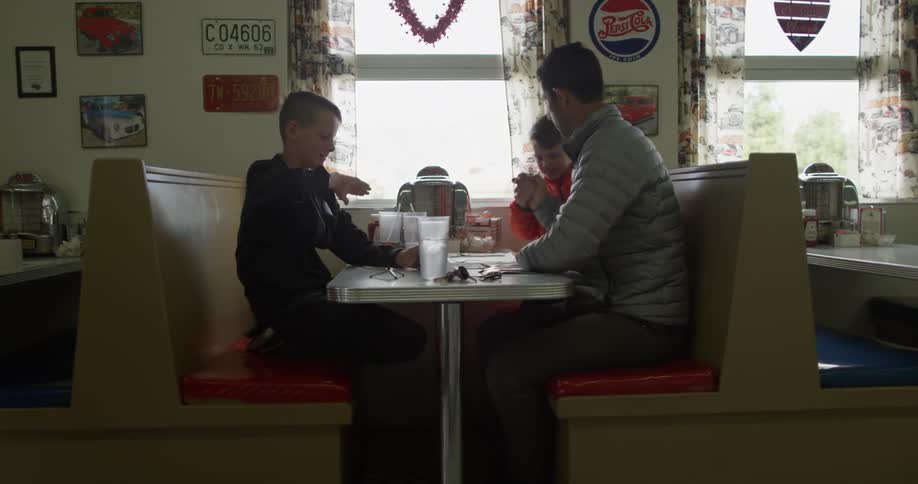 A man and two boys are sitting in a booth at a diner