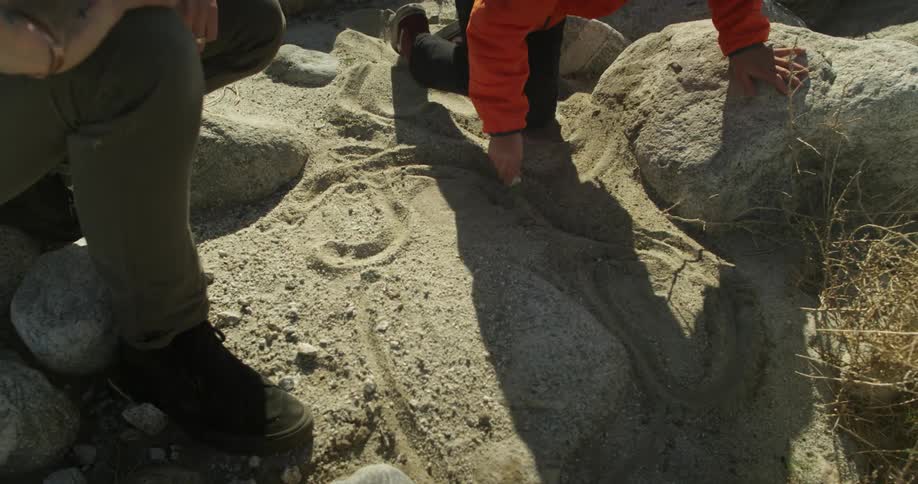 A boy draws in dirt with a rock