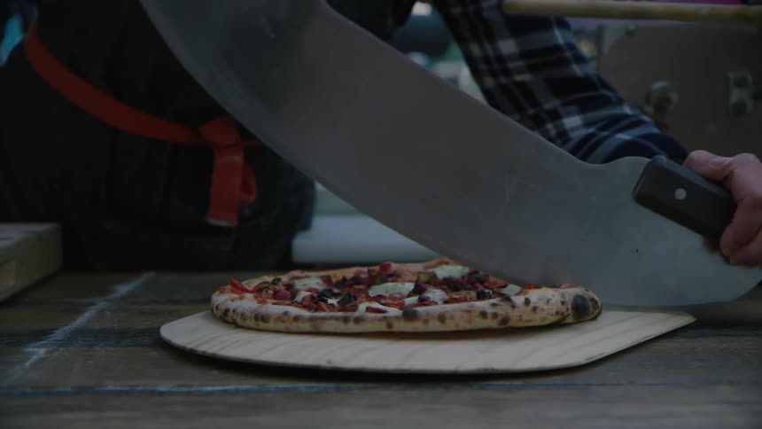 A pizza chef slices a pizza