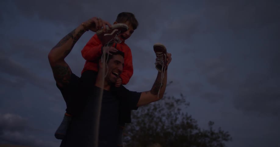 A man pours sand out of a pair of shoes while a boy sits on his shoulders