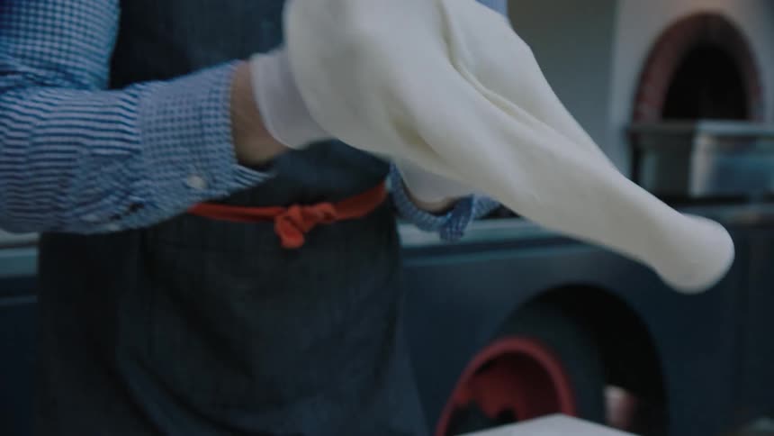 A chef uses his hands to stretch pizza dough
