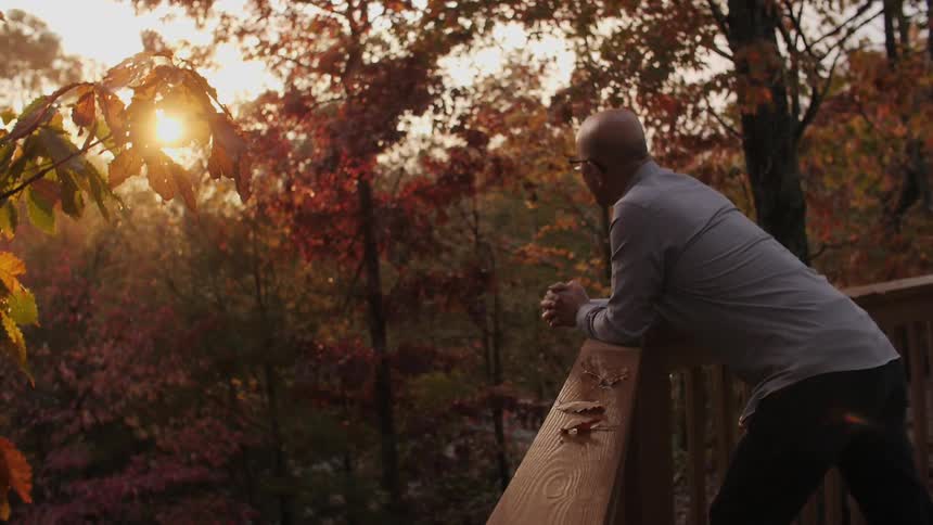 A man looks at fall trees from a deck at sunset