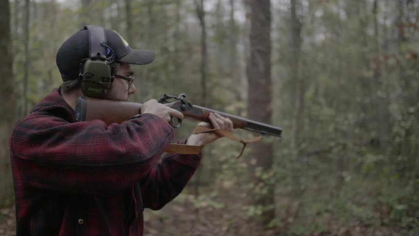 A man aims a rifle in the woods
