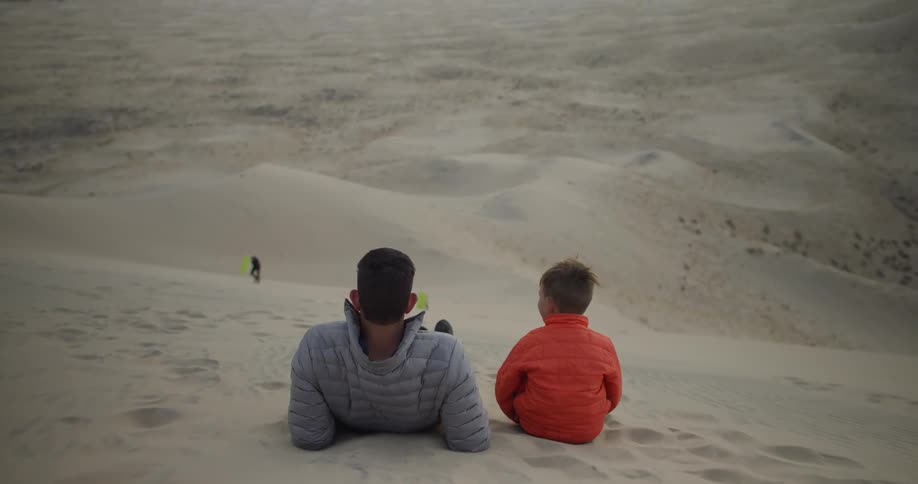 A man and boy lay on a sand dune in the desert