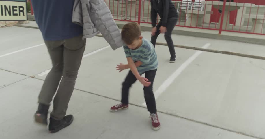A man walks past two boys dancing in a parking lot