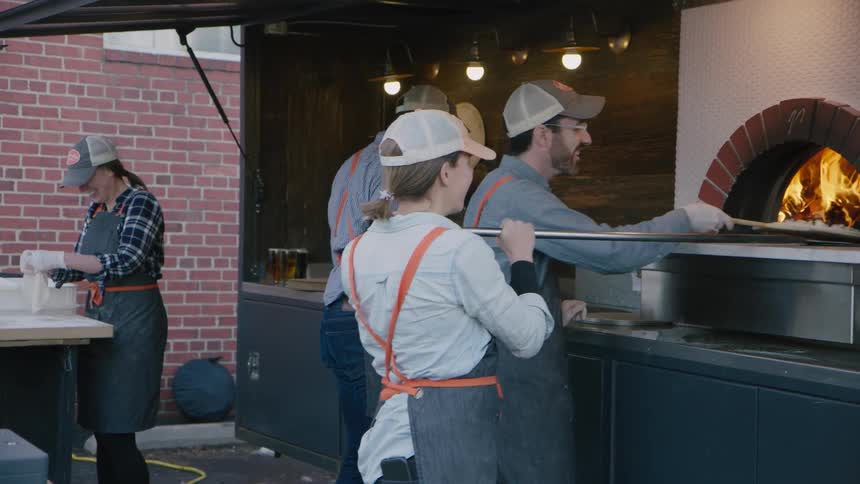 Restaurant workers make pizza in a fire oven