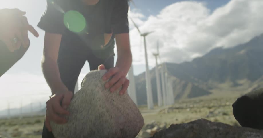 Two young boys pick up heavy rocks by windmills