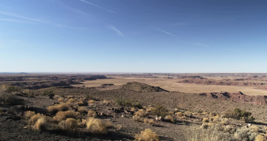 Wisps of clouds and vapor trails hang in a sunny sky over a desert landscape