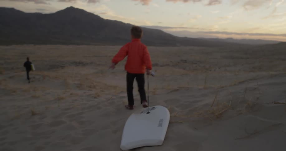 A boy drags his bodyboard over sand dunes
