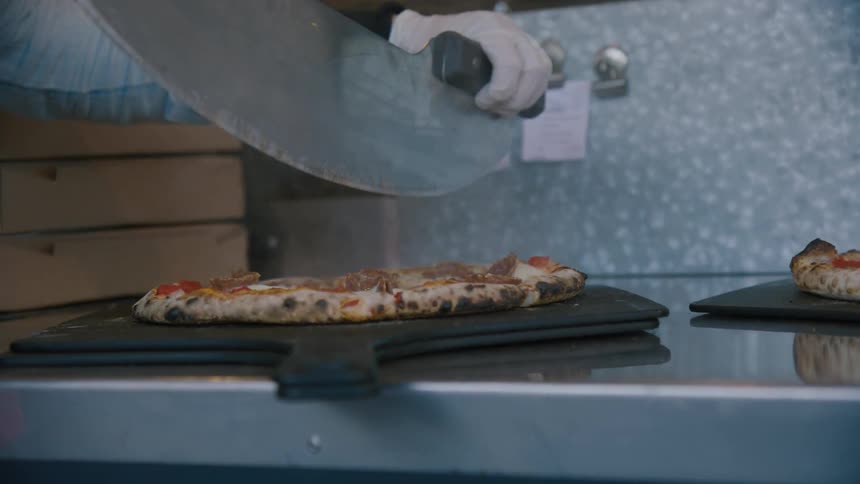 Person cutting a pizza with a large pizza cutter