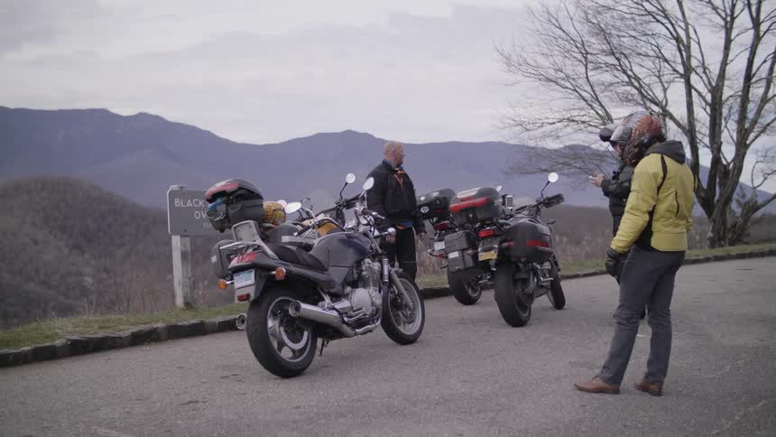 Three people standing near two motorcycles on a road