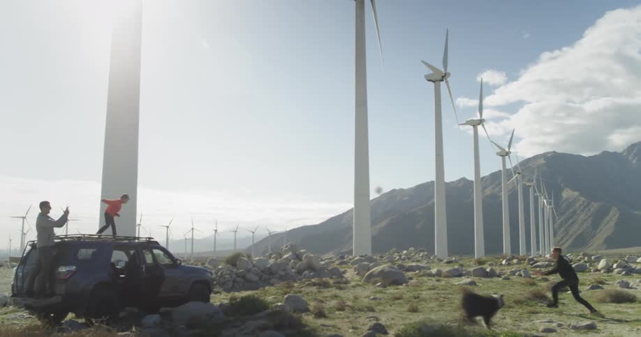 A family and their dog play near windmills