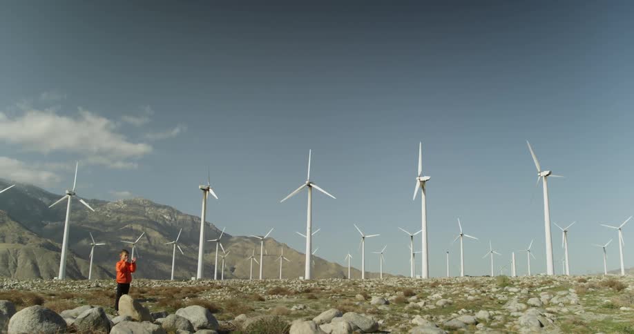 A boy plays near wind turbines on a sunny day