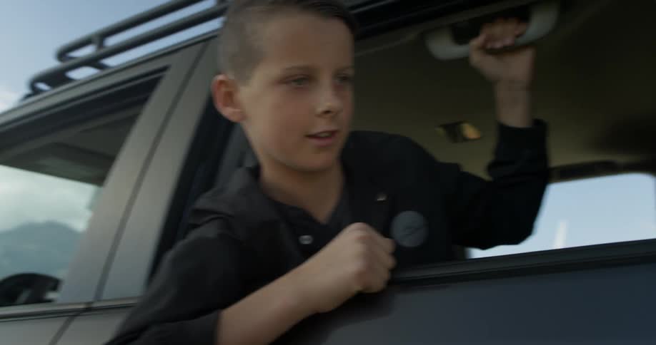 A young boy leans through and looks out of a vehicle window