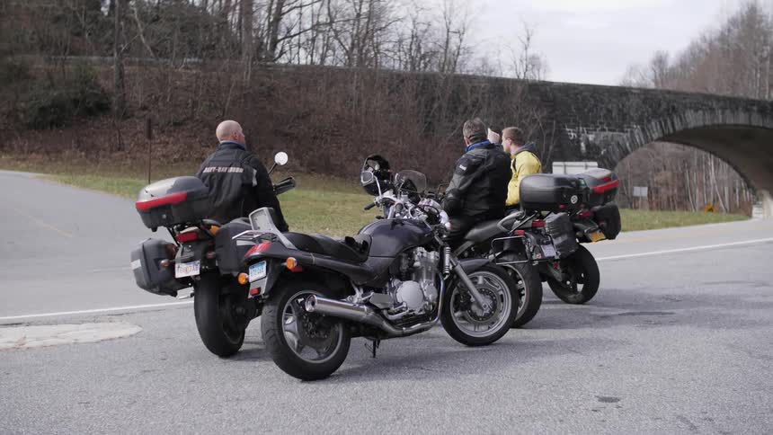 Three men are sitting on their motorcycles in a park