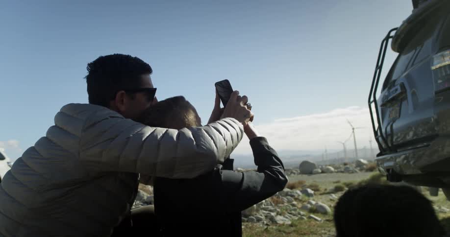 A man helps a boy take a photograph using a smartphone