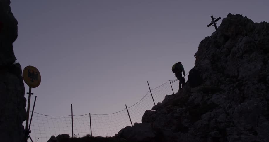 A hiker climbs toward the cross on a rocky peak