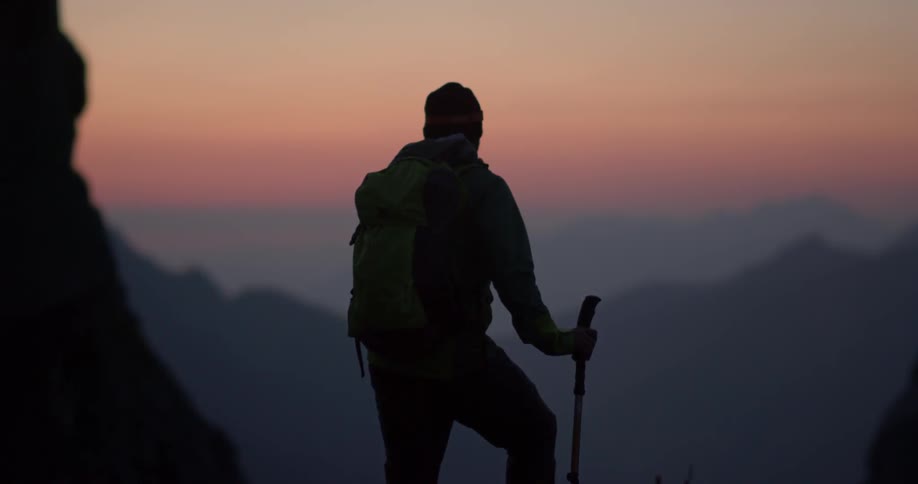 Man carrying a walking stick looks at hills at sunset