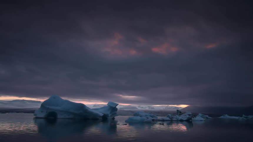 Water flows around icebergs at dusk on a stormy day