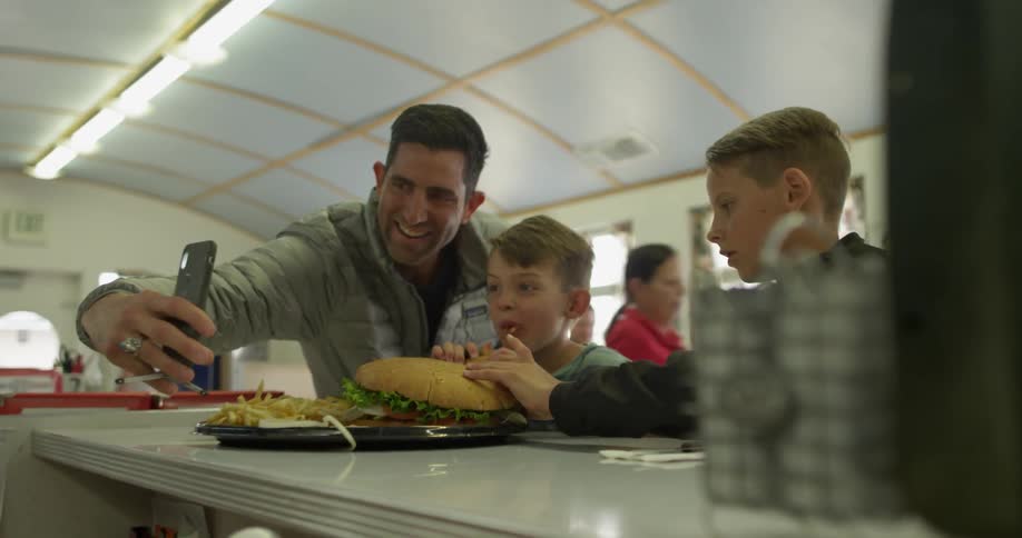 A man and two boys take a photograph while eating in a diner