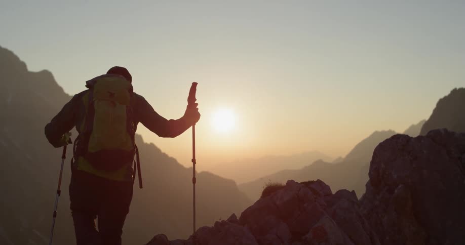 Man wearing a backpack hikes up a rocky mountain with two walking sticks