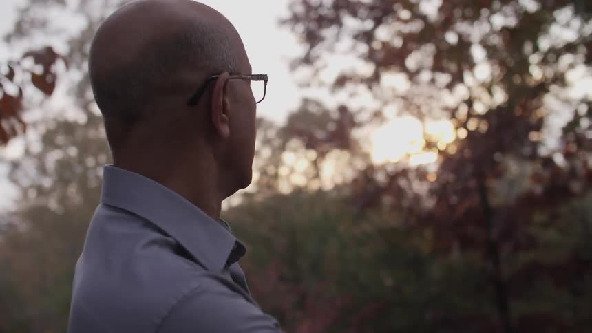 A man looks out at fall trees at sunset