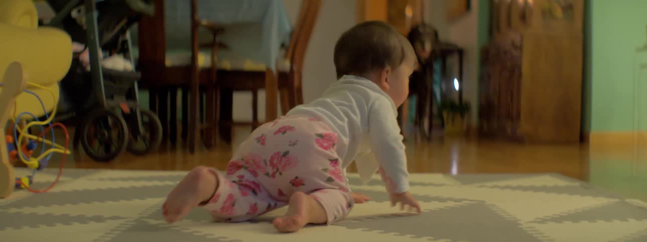 A baby is crawling and exploring on a living room floor during the day
