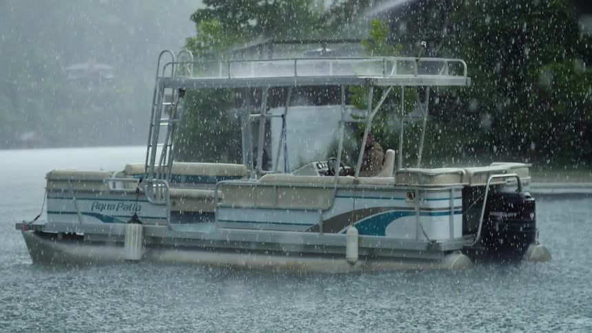A boat sits still on a lake as rain falls all around it