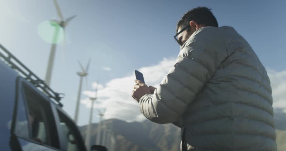 A man holding his cell phone helps his son out of the car