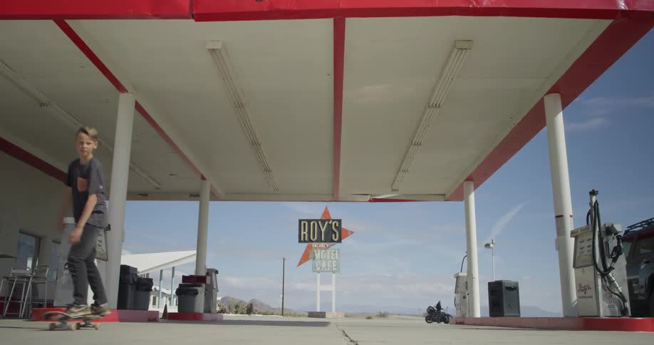 A boy skateboards near gas pumps at a gas station