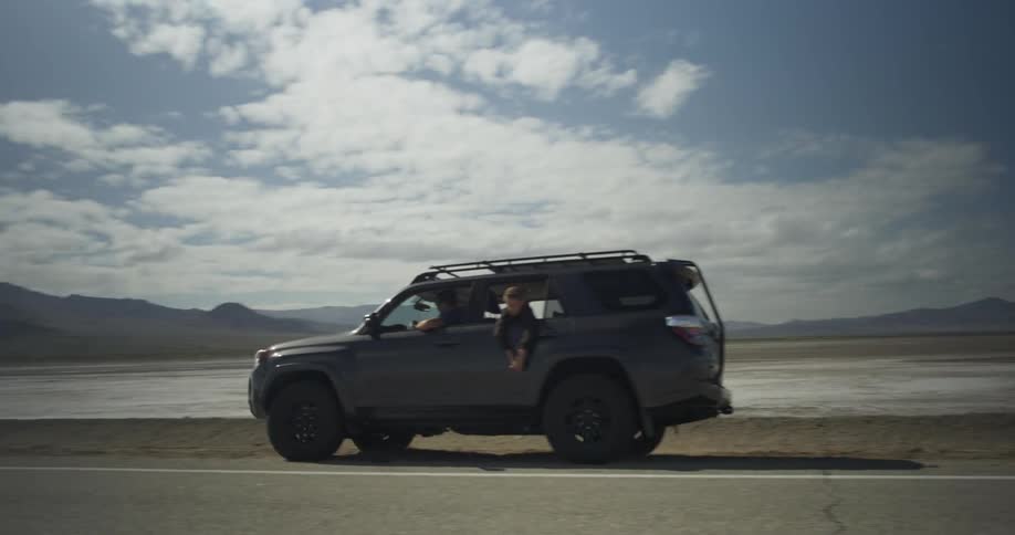 A car with a young boy leaning out the window pulls over on a rural road