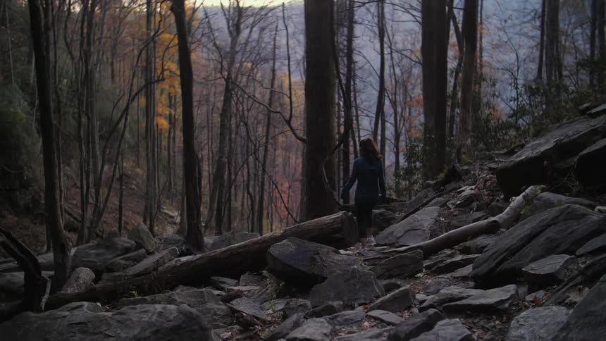 A woman walks over large rocks in the woods